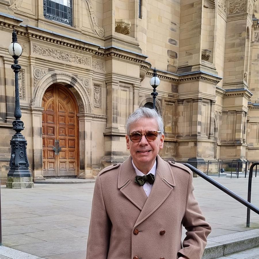 Emre Araci stands outside the McEwan Hall. He wears sunglasses, a smart camel coat and a bow tie.