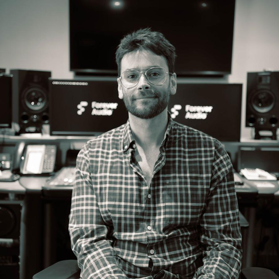 Fraser sits in a music studio, with a desk, monitors and computers behind him.