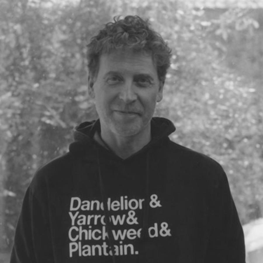 A black and white image of Martin Parker, smiling to camera and wearing a black hooded jumper with white text on it.