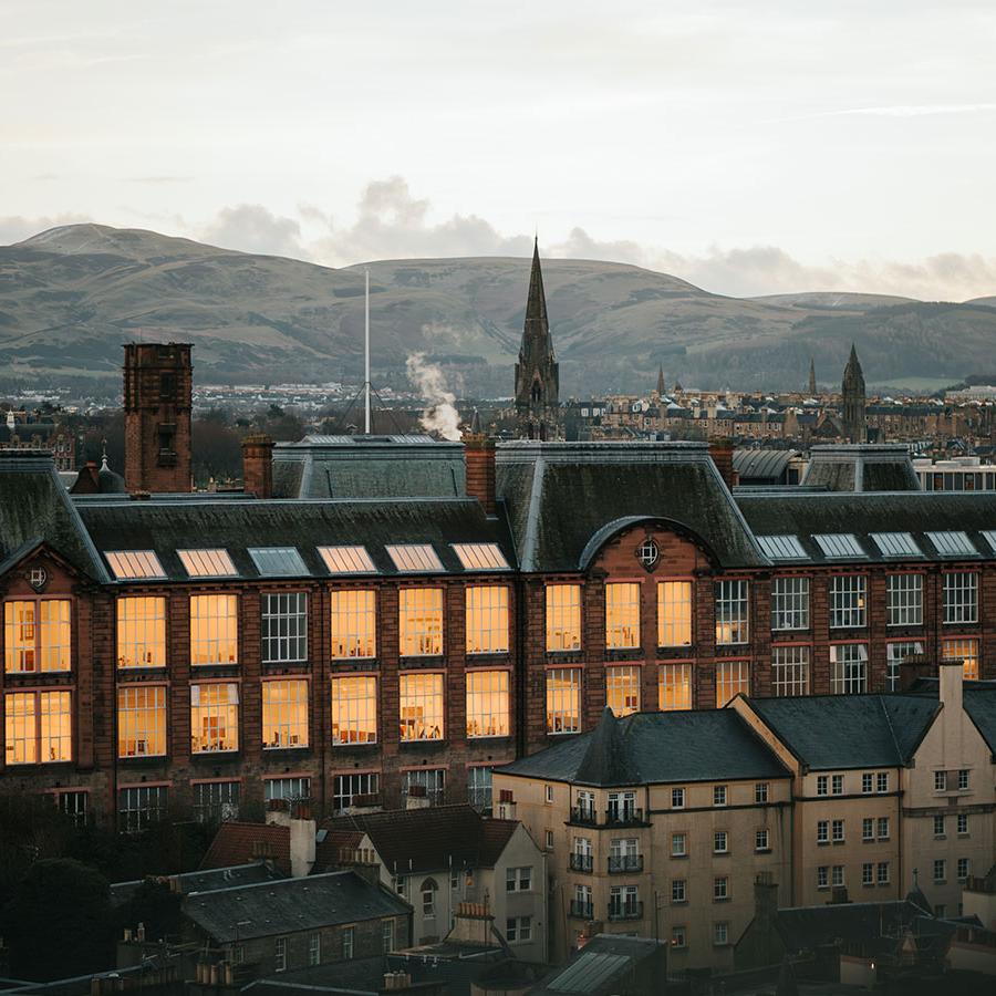 A view of ECA's Main Building on Lauriston Place, with the many large studios lit up. The Pentland hills can be seen in the background.