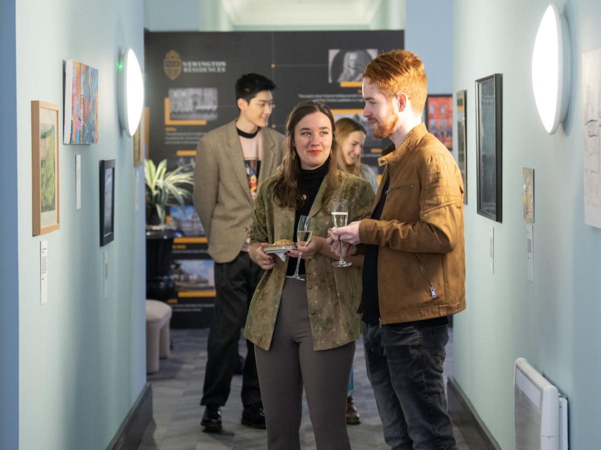 Two students viewing artwork on display on a wall.