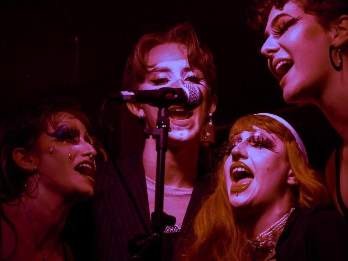 Four performers singing into a shared microphone