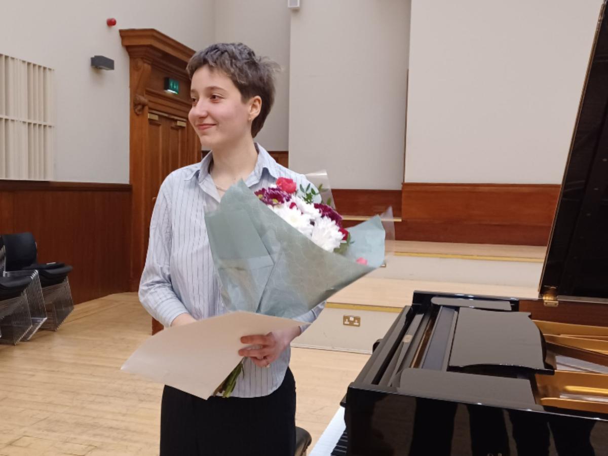 A photo of first prize winner Paloma holding a bouquet of flowers at a piano