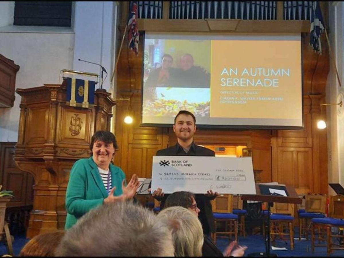 Two people presenting a large charity cheque in a church hall