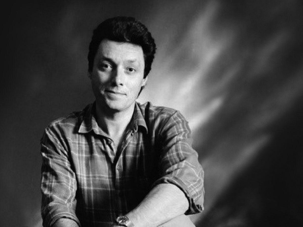 A black and white image of a man wearing a shirt, smiling and looking at the camera.