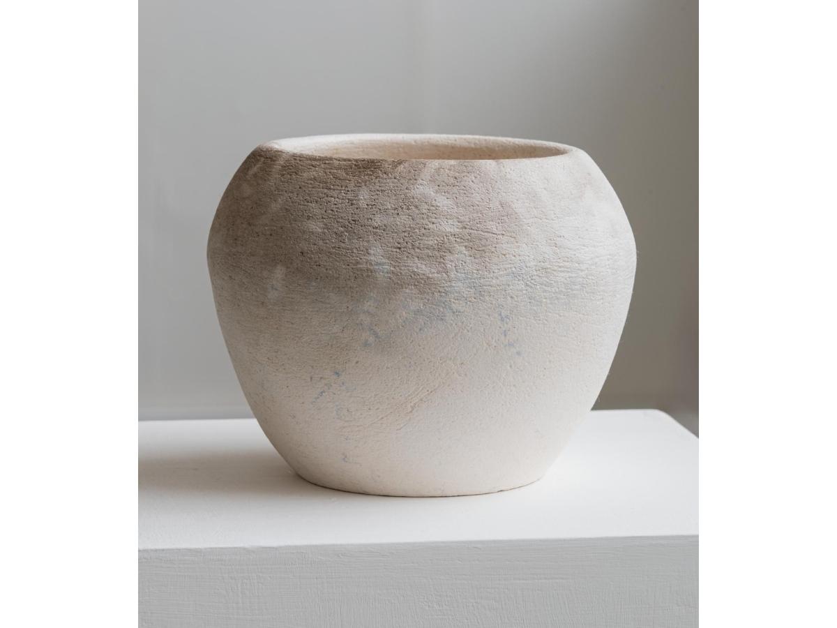 A circular pot. It is is white, with some shading and patterns towards the top.
