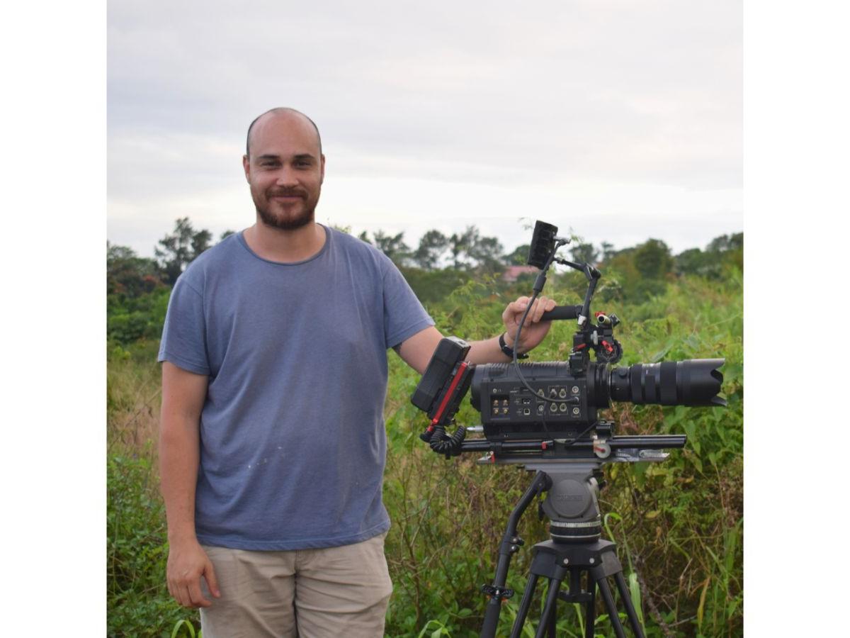 Andrew stands beside the camera, in a field of lush greenery