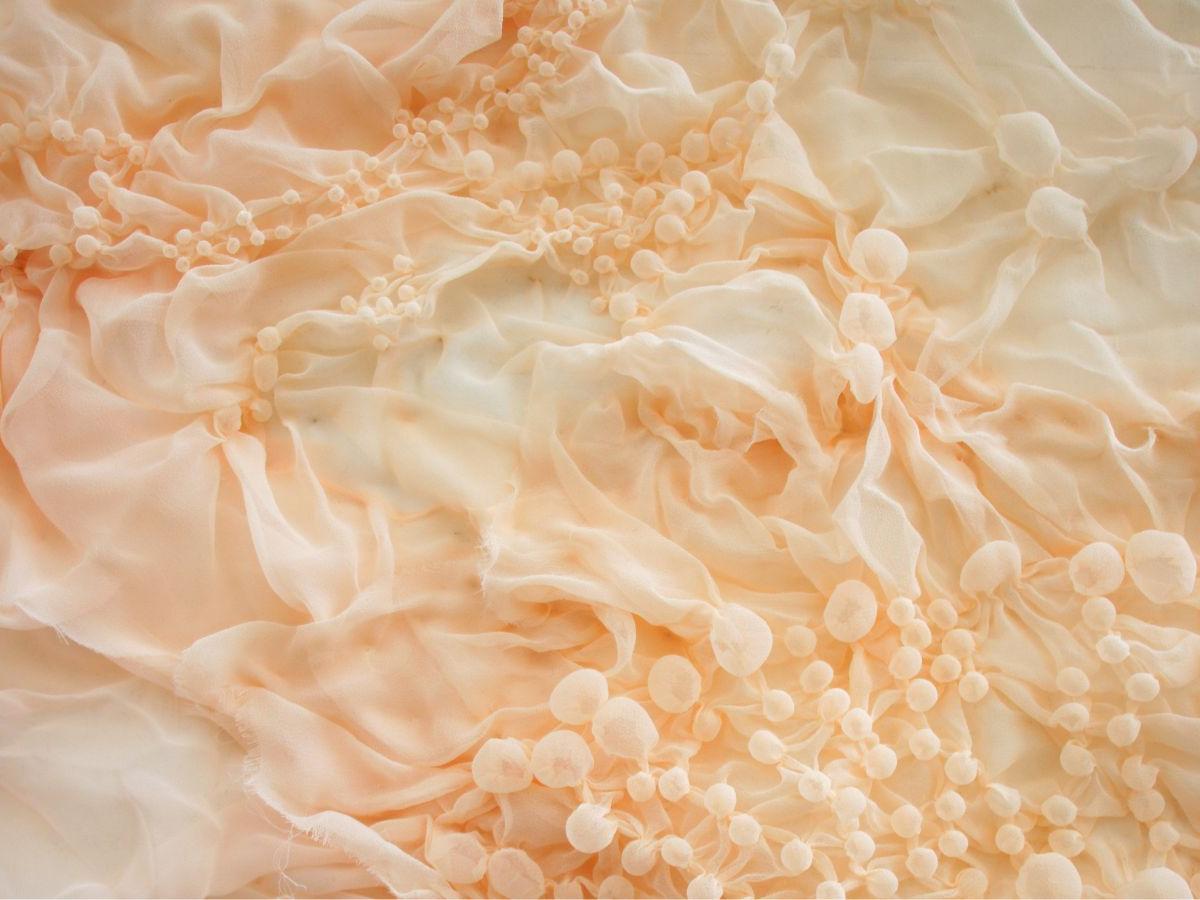 Pale, gauzey, ruffled creamy pink fabric is rouched up to form multiple little bubbles and waves.