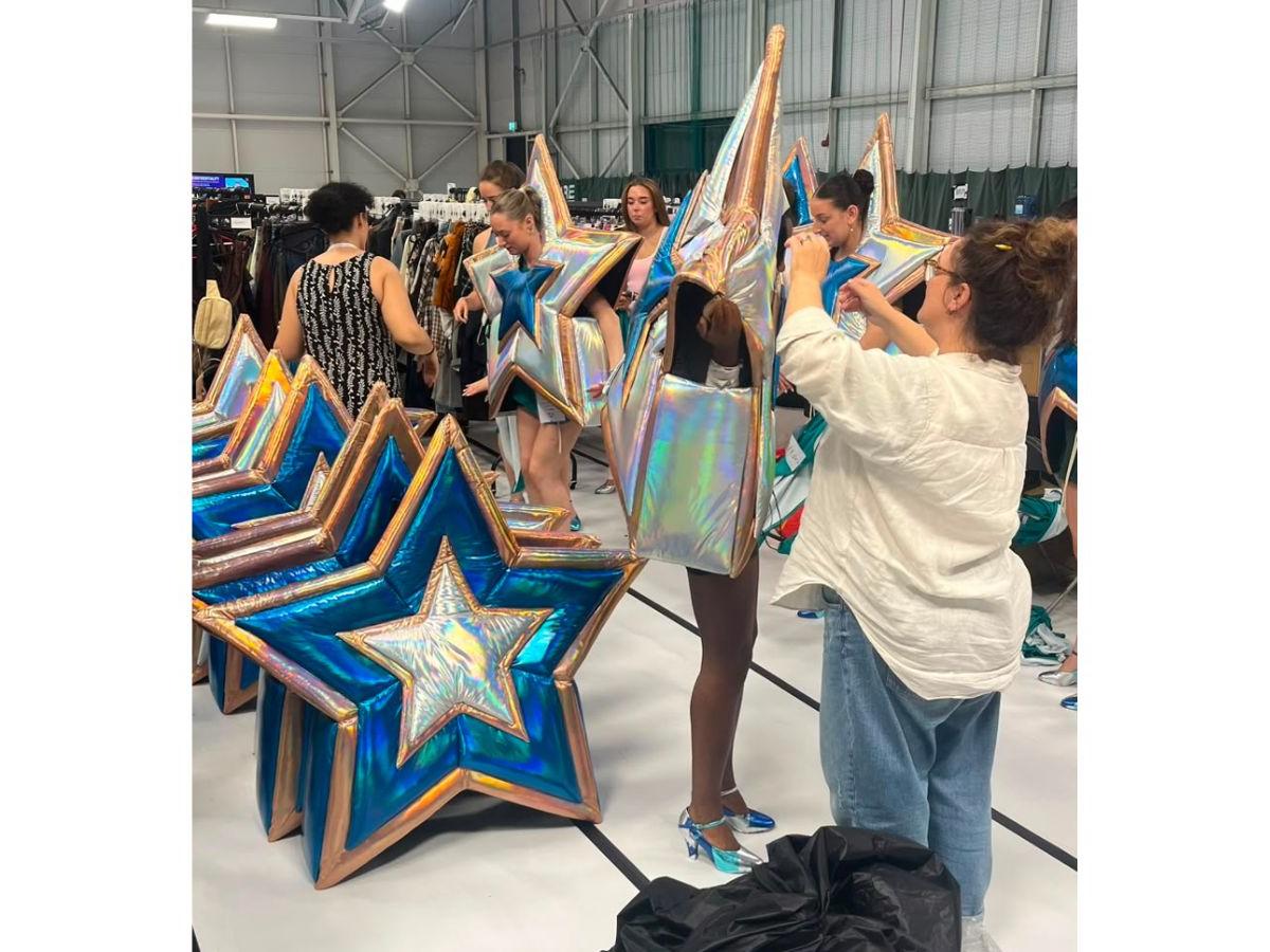 In a large warehouse, costume staff help performers into star-shaped, blue and silver costumes.