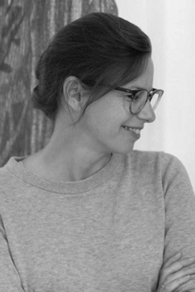 A black and white image of a person looking sideways, wearing glasses and a plain jumper.