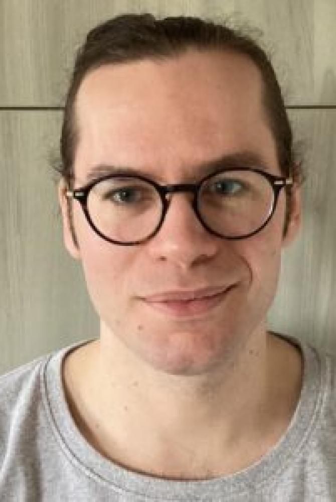 A person with dark hair, wearing glasses and smiling to the camera.