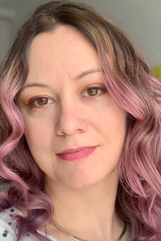 A person with long pink hair, smiling at the camera.
