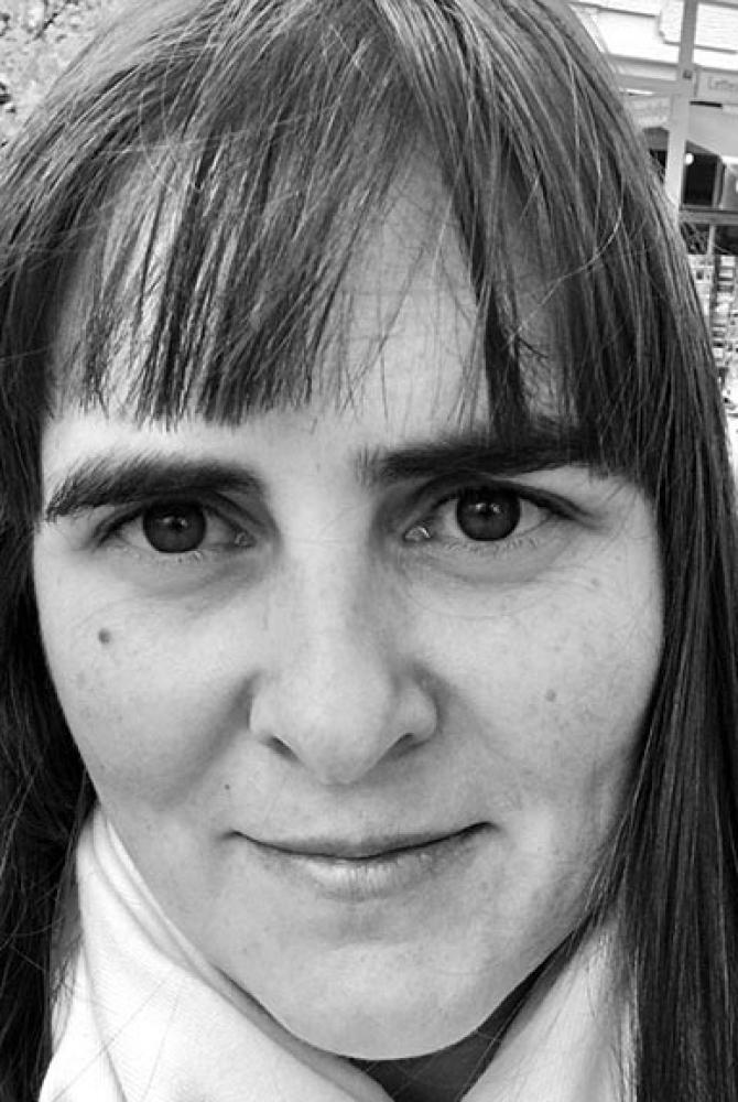 A black and white image of a person with dark hair, wearing a white scarf and looking at the camera.