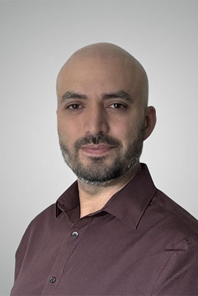 A bald person with a dark beard. They're half turned to the camera, wearing a maroon shirt.