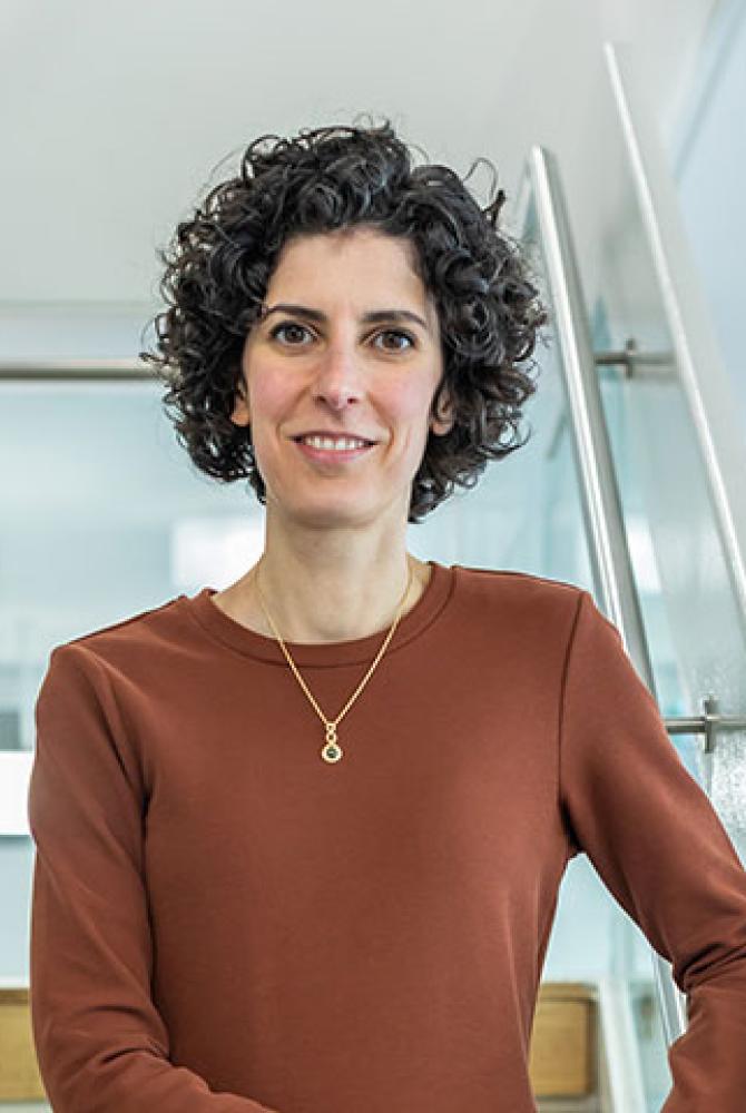Caterina standing on a set of stairs, wearing an orange/brown coloured dress. They are smiling at the the camera.