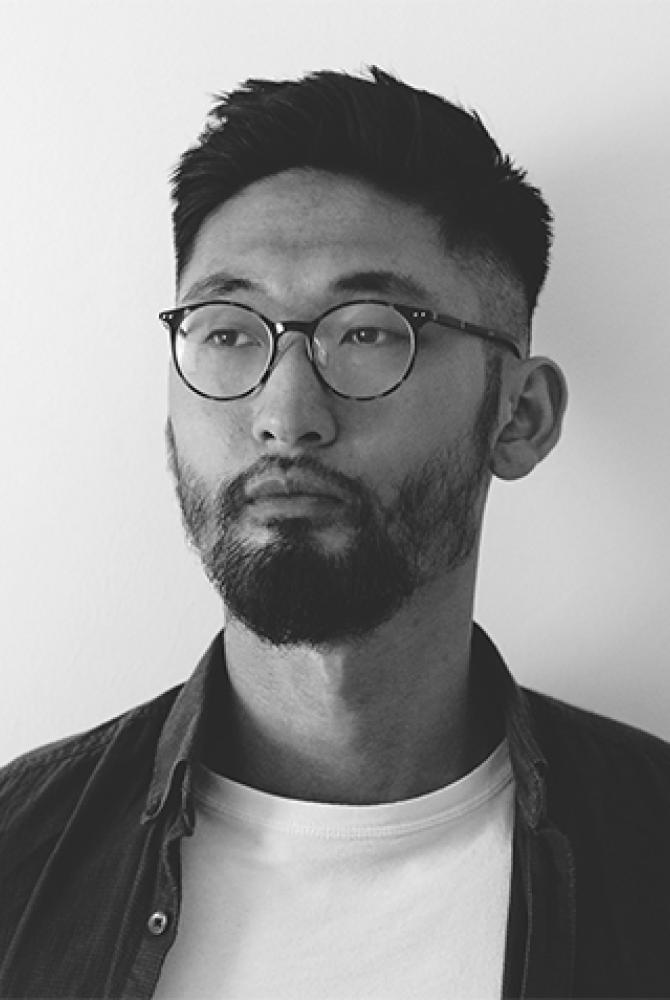 A black and white photo of Thorranze, wearing a white tshirt and dark shirt, glasses, and looking just off camera.