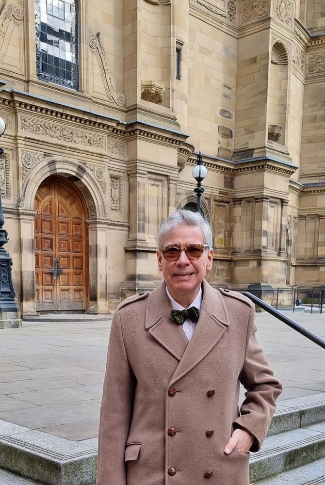 Emre Araci stands outside the McEwan Hall. He wears sunglasses, a smart camel coat and a bow tie.