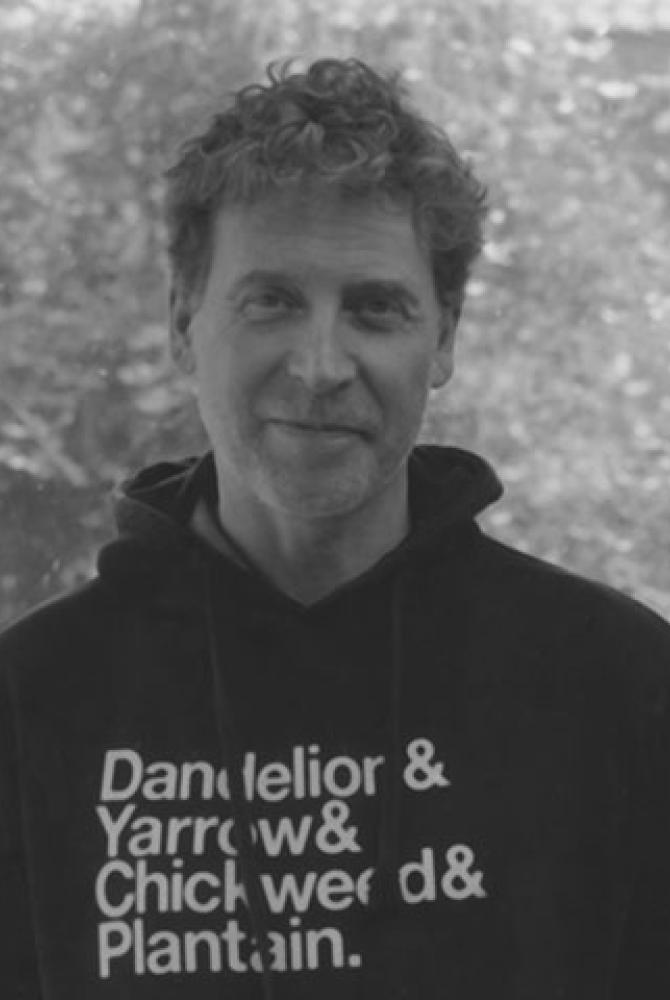 A black and white image of Martin Parker, smiling to camera and wearing a black hooded jumper with white text on it.