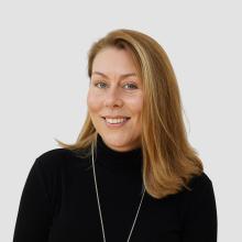 A person with shoulder length blonde hair, wearing a black high necked top