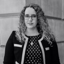 A black and white image of a person with long, curly hair, wearing a black and white jacket and polka dot dress.