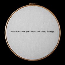 A crossstitch ring with embroidered text reading are you sure you want to shut down?