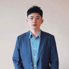 A person with short dark hair, glasses, wearing a light blue shirt and dark blue jacket.