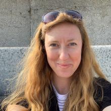 A person with long, auburn hair, wearing glasses on their head and smiling at the camera.