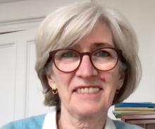 A person with short, grey hair, wearing glasses and smiling at the camera