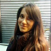 A person with long dark hair, smiles at the camera