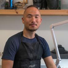 Glass and ceramic artist Choi Keeryong sitting in their studio.