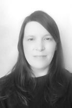 A person with long dark hair and a dark jumper, looks directly at the camera.