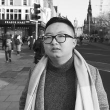 A person stands on Edinburgh's Princes Street, with the Scott Monument and Christmas ferris wheel in the background.