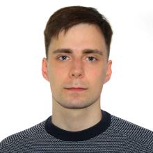 A person with short brown hair, wearing a navy blue top with white stitch detailing on it