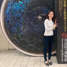 Student Jiaying Gu standing by a sign, with an image of a galaxy behind.