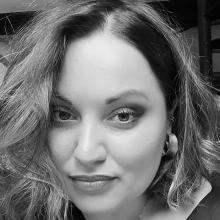 A black and white image of a person looking into the camera. Their hair is short but curly and they're wearing big hoop earrings.