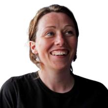 A head and shoulders photograph of Sue. She's wearing a black top, smiling and looking up towards the top right of the image