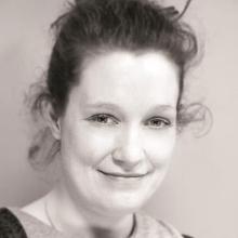 A sepia toned image of a person with their hair tied back, smiling at the camera.