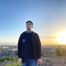 A person standing on Calton Hill, with a view of Edinburgh behind them and the sun setting in the distance.