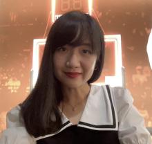 A person with should length dark hair, wearing a white and black blouse with a sailor style collar. They are smiling at the camera.