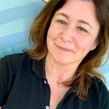 A person with short brown hair, wearing a blue shirt, smiles to the camera.