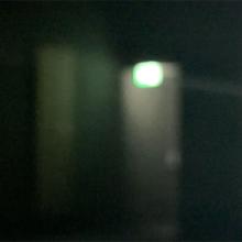 A still from a film which shows a blurred emergency exit light above a door in a dark corridor.