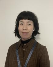 A person with short, dark hair, wearing a brown checked shirt and smiling to the camera.