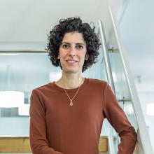 Caterina standing on a set of stairs, wearing an orange/brown coloured dress. They are smiling at the the camera.