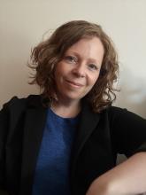 A person with short, curly, light brown hair, smiles to the camera.
