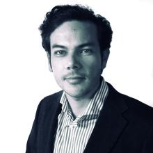 A black and white image of Edgar Gomez wearing a striped shirt and black suit jacket. He looks straight into the camera.
