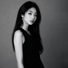 Minshu Chen has long dark hair and stands to the side but looks to the camera.