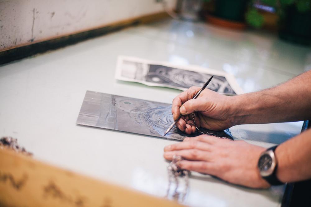 A pair of hands painting on a piece of work in the printmaking studio