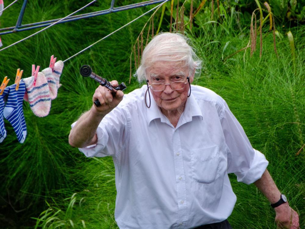 A person in a light blue shirt holding a walking stick in the air in a garden
