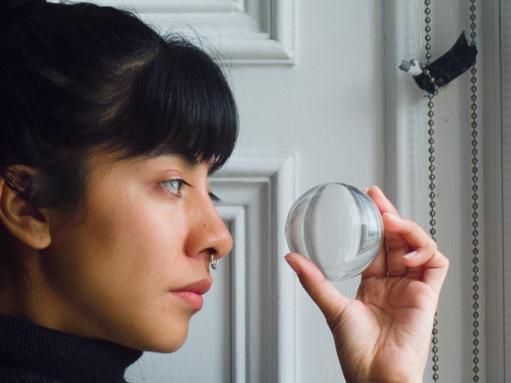 A person stands by a window, looking at the glass ball in their hand.