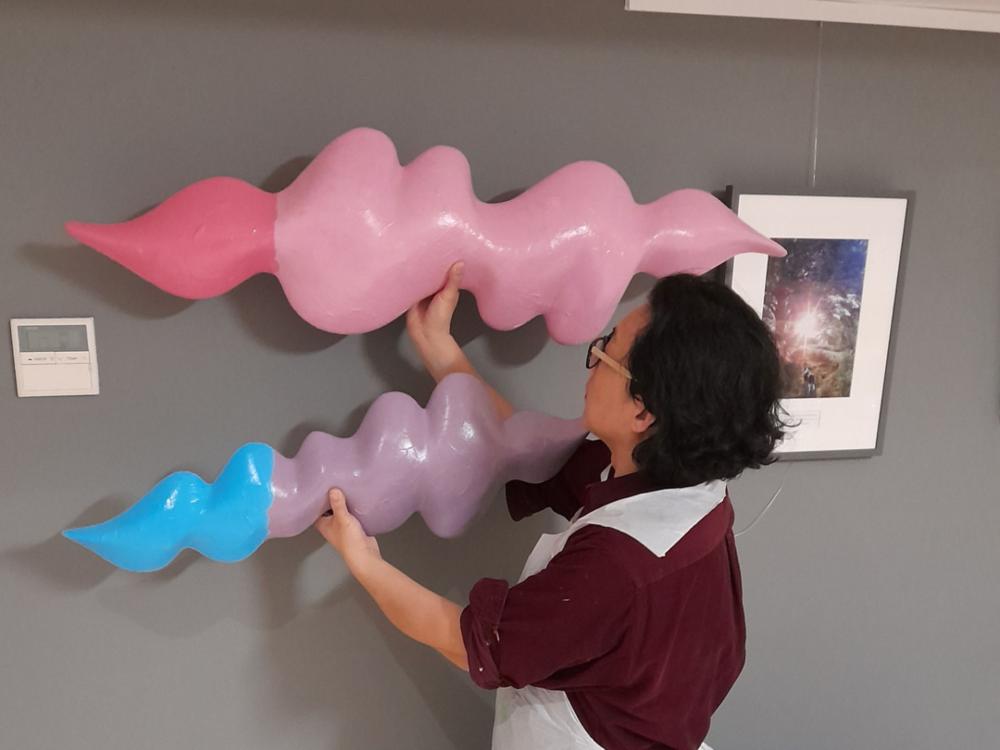 A photo of Xeuchang positioning two of the artworks on a wall.